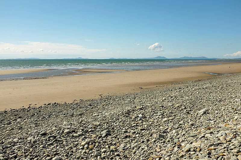 fairbourne-beach-pebbles-lead-down-to-a-deserted-sandy-beach-and-sea-with-mountains-in-the-distance