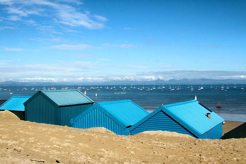 aberdaron-beach-blue-beach-huts-in-the-sand-look-out-over-the-sea-with-yachts-and-mountains-in-the